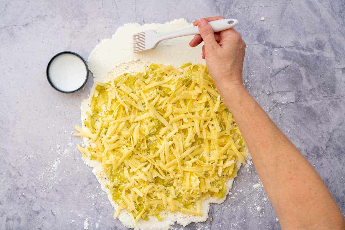 Water being brushed over pizza dough with a pastry brush.