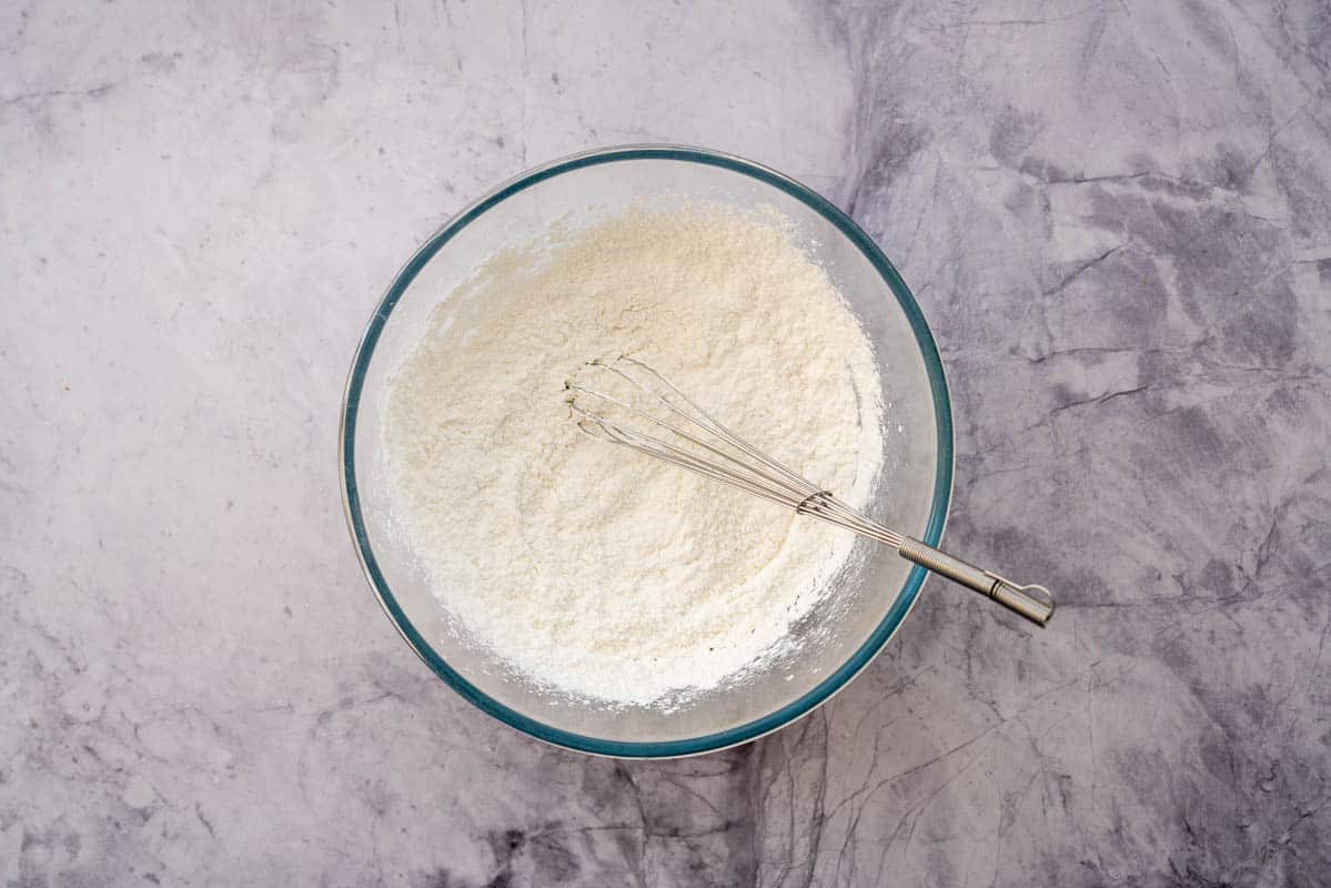 Dry ingredients in a glass mixing bowl with a whisk resting on the side.