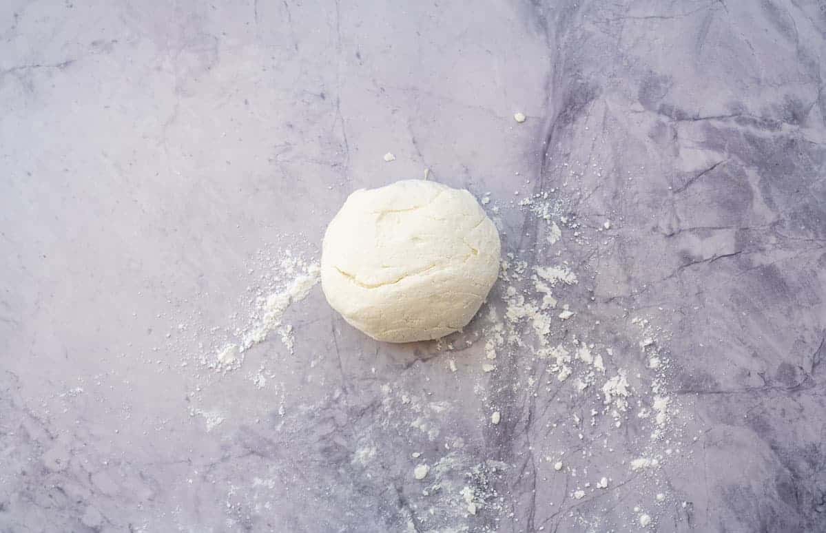 A ball of dough on a floured marble bench top.
