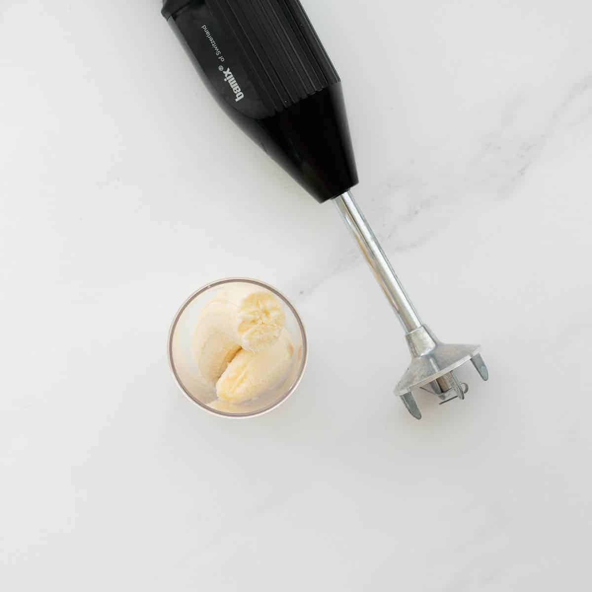 A stick blender beside a container with peeled and halved bananas