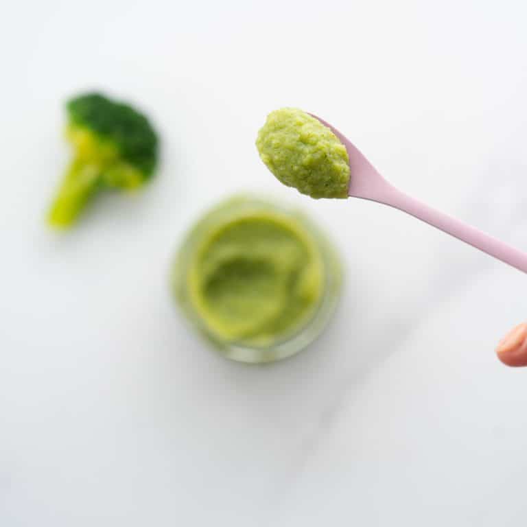 A spoonful of broccoli puree being held above a glass jar of puree.