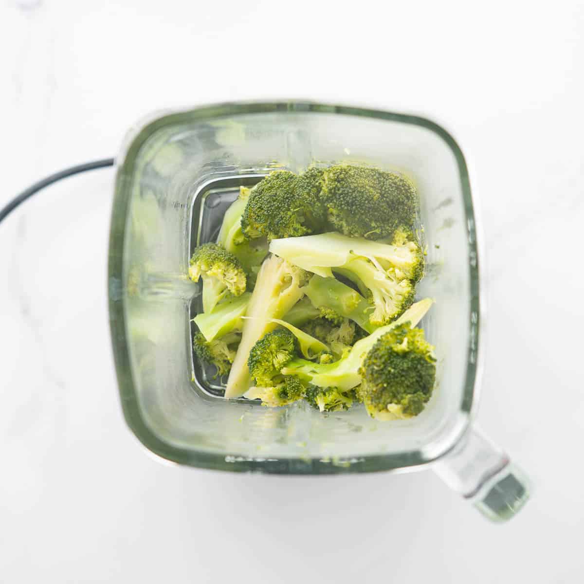 Steamed broccoli florets in a glass blender jug.