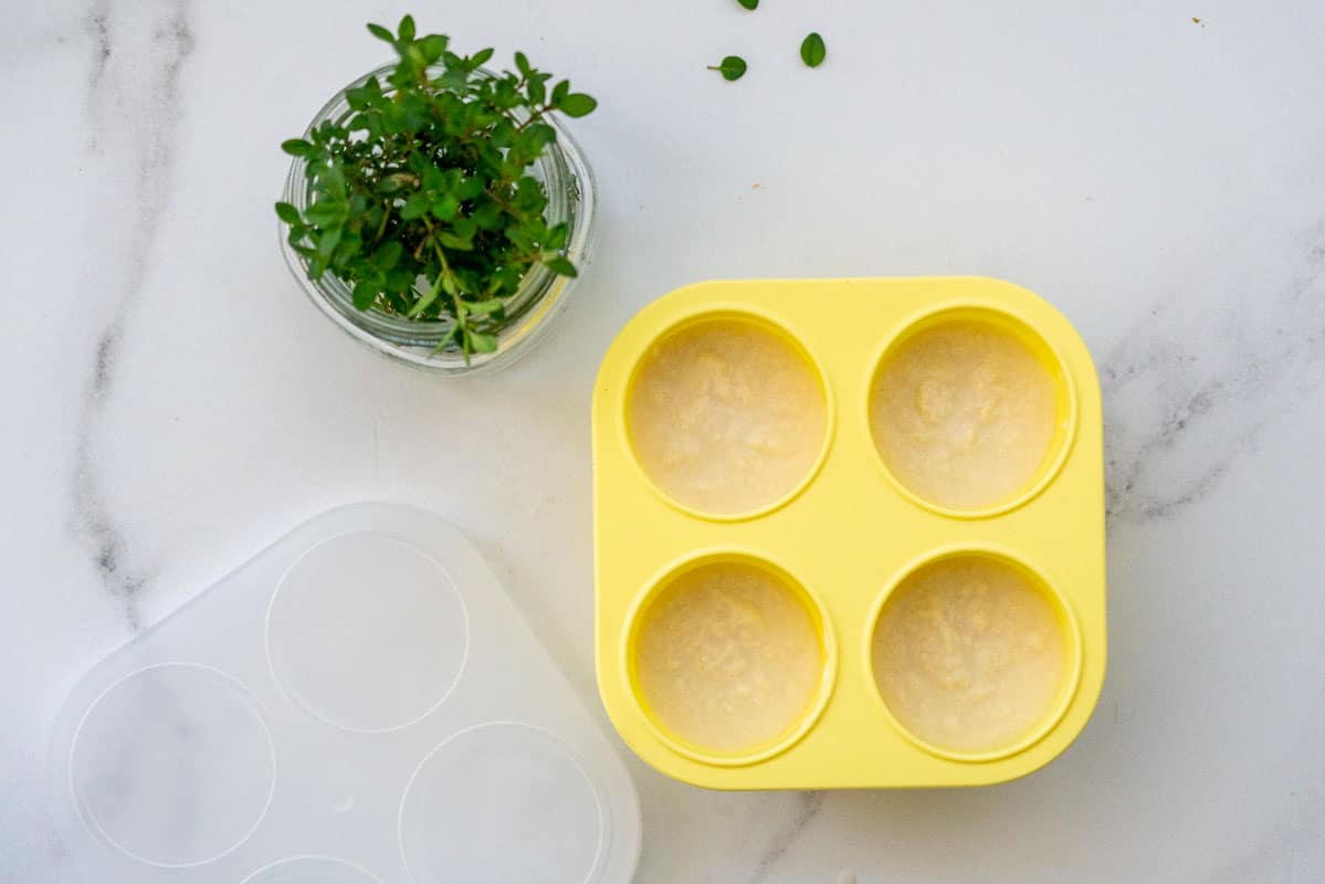 A yellow baby food tray filled with chicken on a marble bench top.