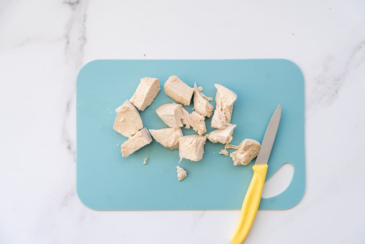 Diced chicken breast on a light blue chopping board.