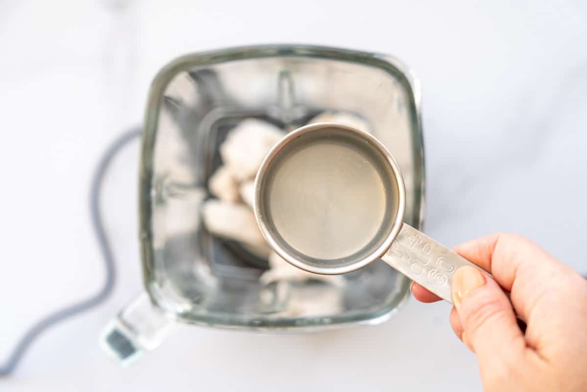 A one quatrer cup measure of liquid being held above a blender jug of cubed poached chicken