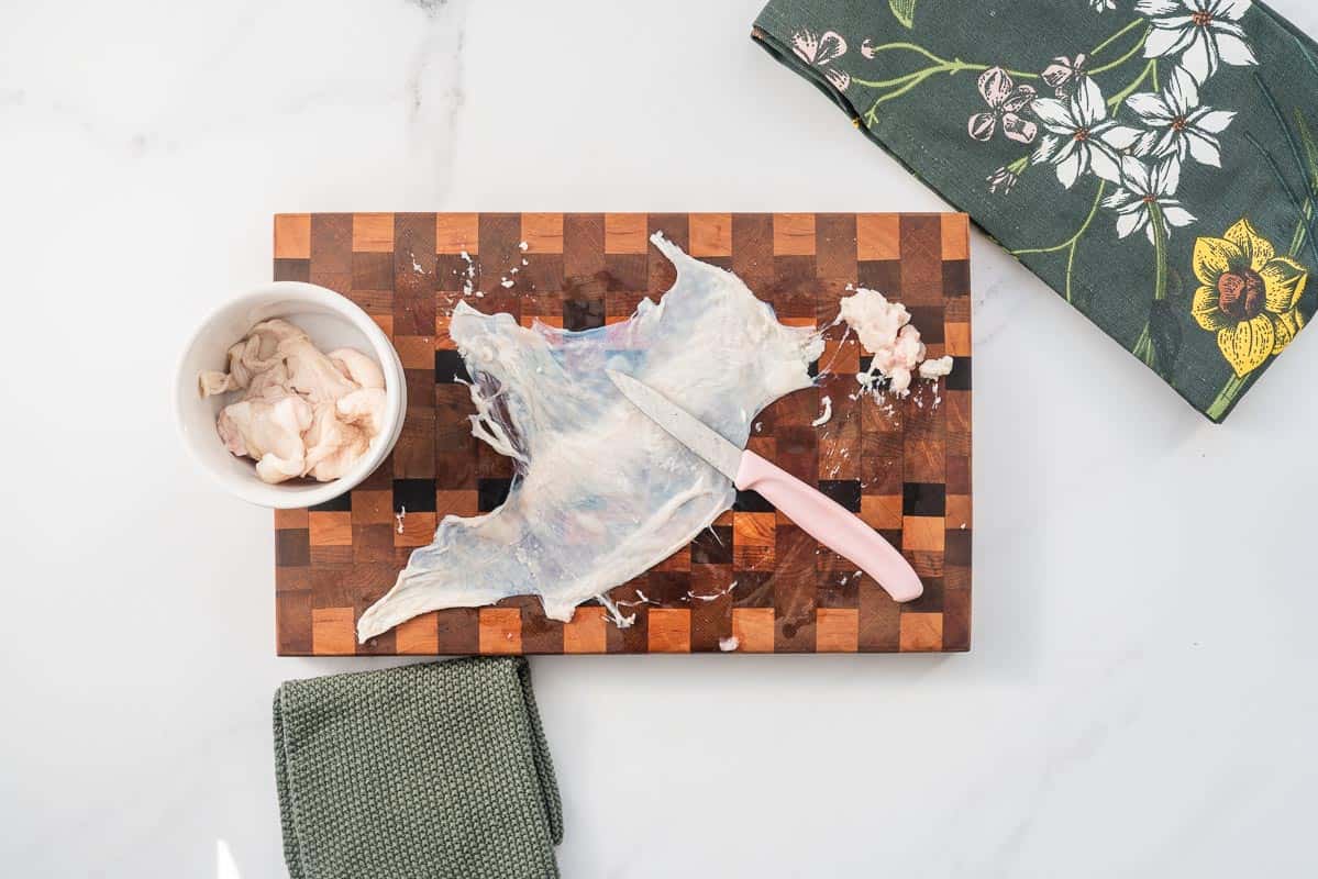 Chicken skin stretched on a wooden chopping board, excess fat has been scraped off.