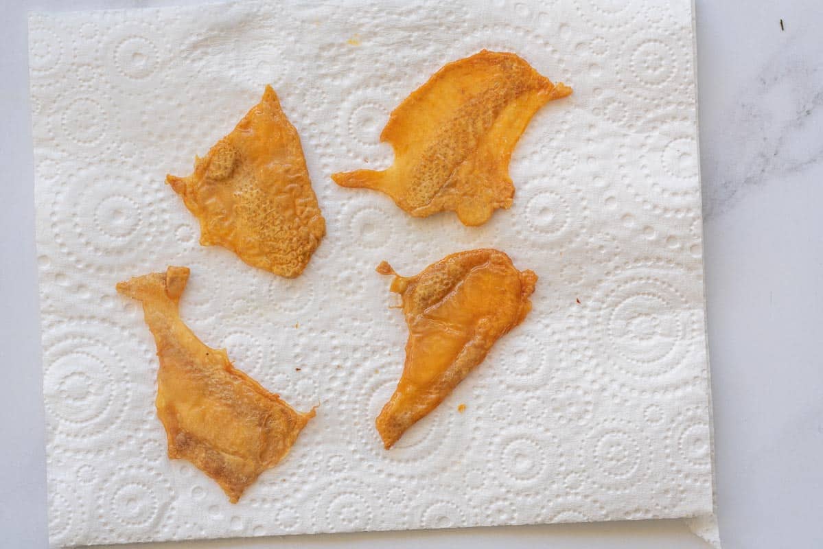 Golden brown chicken skins laid out on a piece of paper towel.