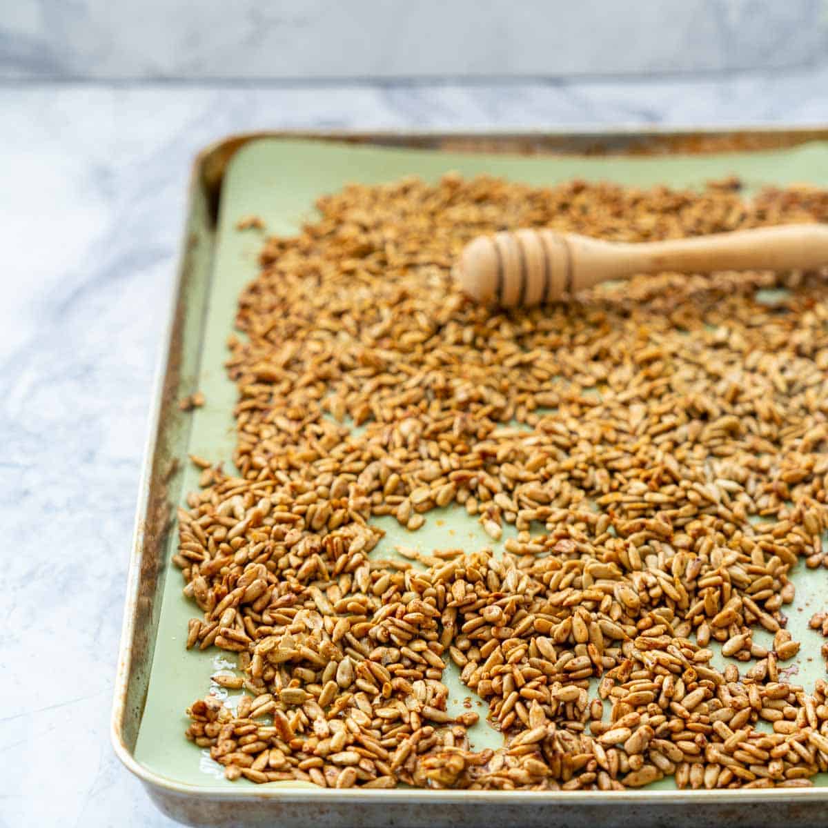 Over tray with a green silicone liner with the coated sunflowers and the honey dripper stick