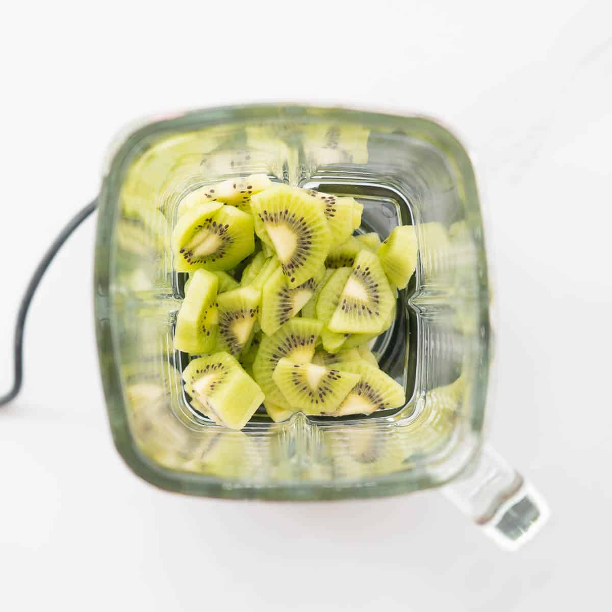 Slices of kiwi in a square glass blender jug.
