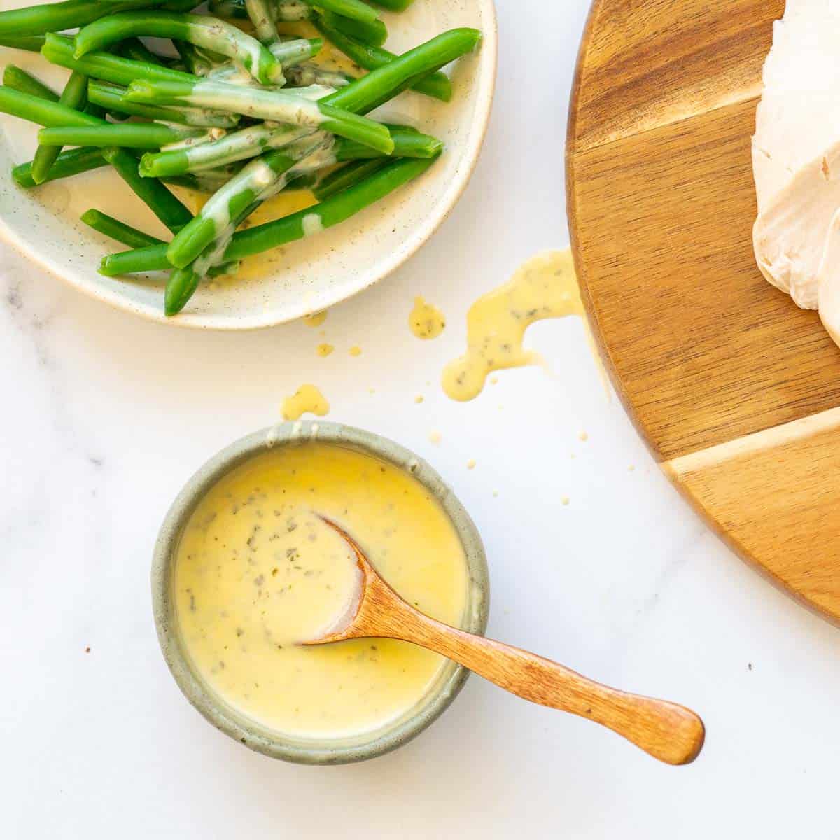 A small green ramekin of yellow sauce with a wooden spoon, and dripts of sauce on the table top.