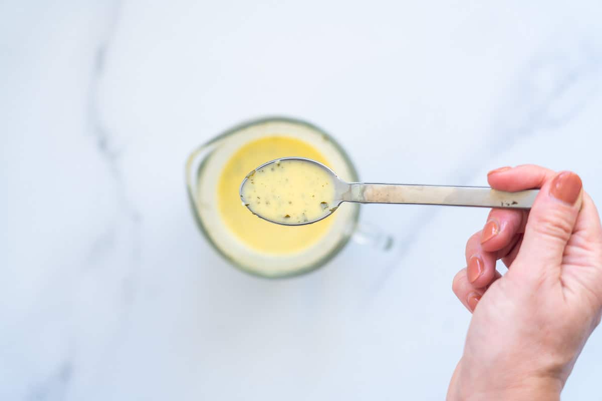 A spoonful of yellow sauce being held above a microwave jug of sauce.