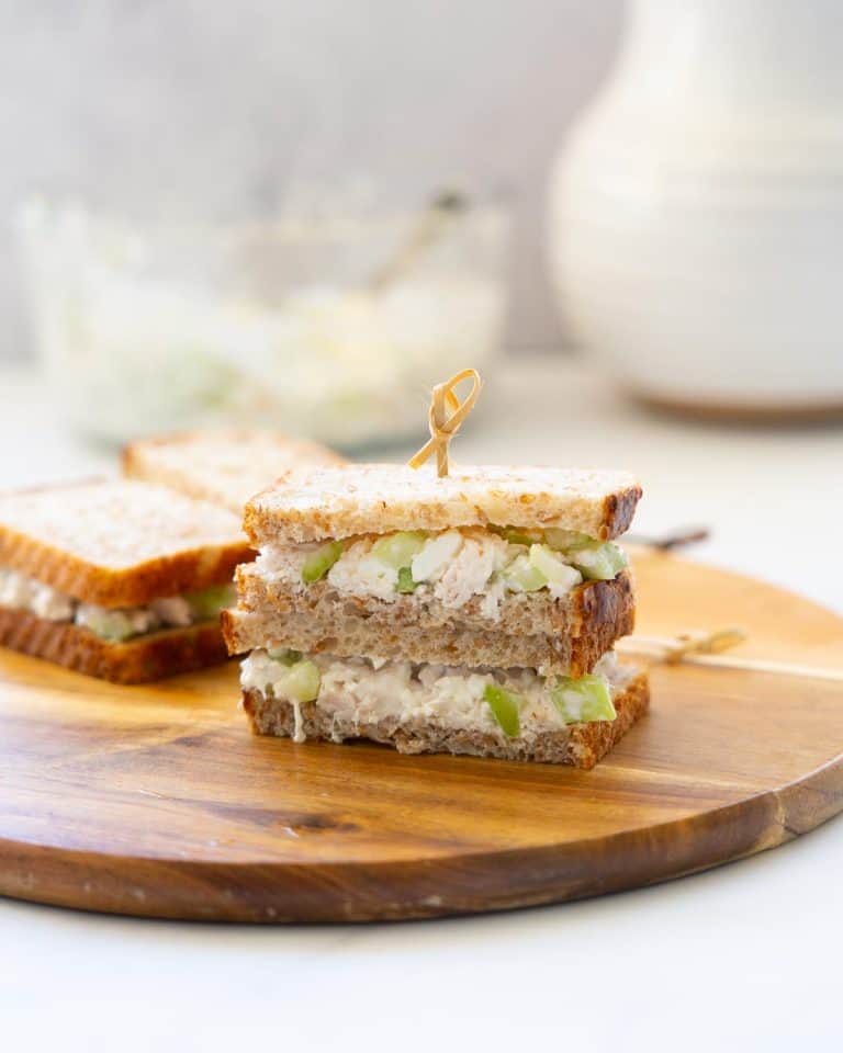 Shredded chicken sandwiches stacked on a wooden board and held together with a bamboo toothpick.