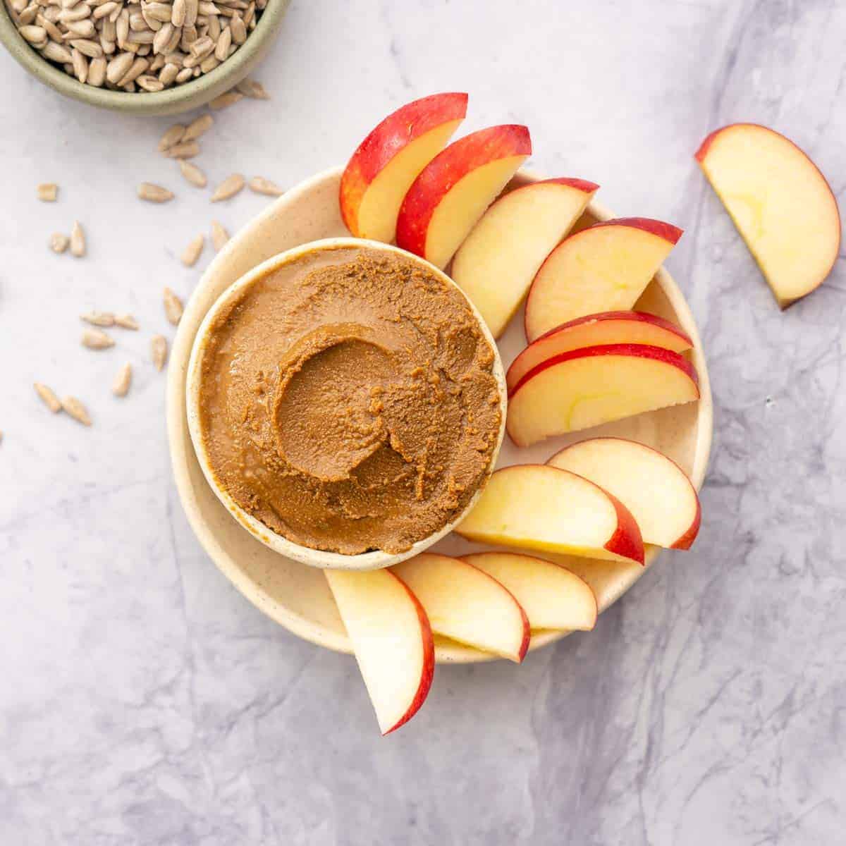 A plate with red apple slices and a small bowl of sunflower seed spread for dipping