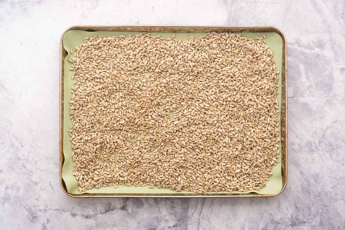 An oven tray with silicone liner and a layer of sunflower seeds ready to roast