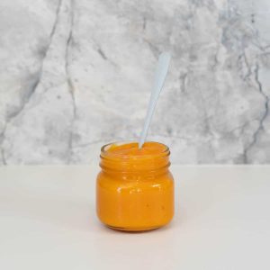 A jar filled with orange puree in front of a marble splash back.