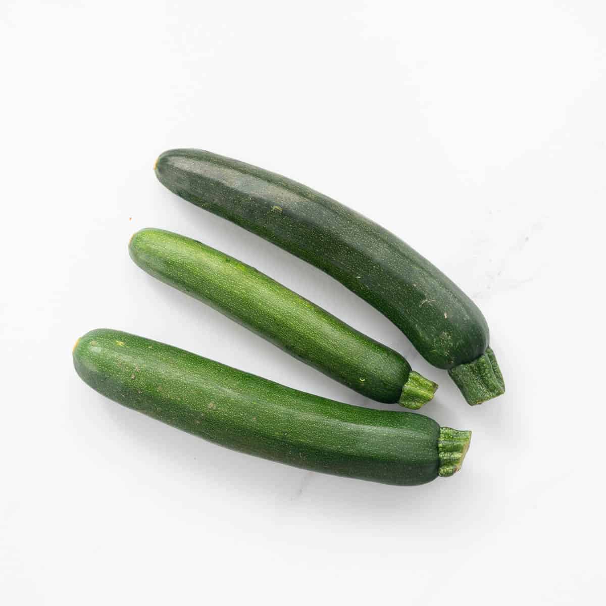 Three zucchini lying on a white marble bench.