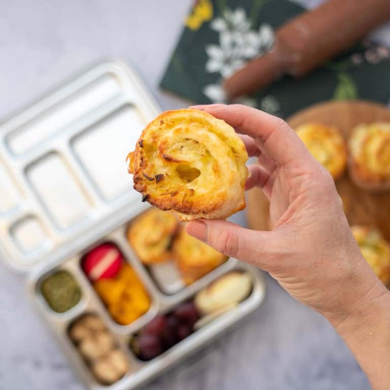 A scroll being held above a packed stainless steel lunchbox.