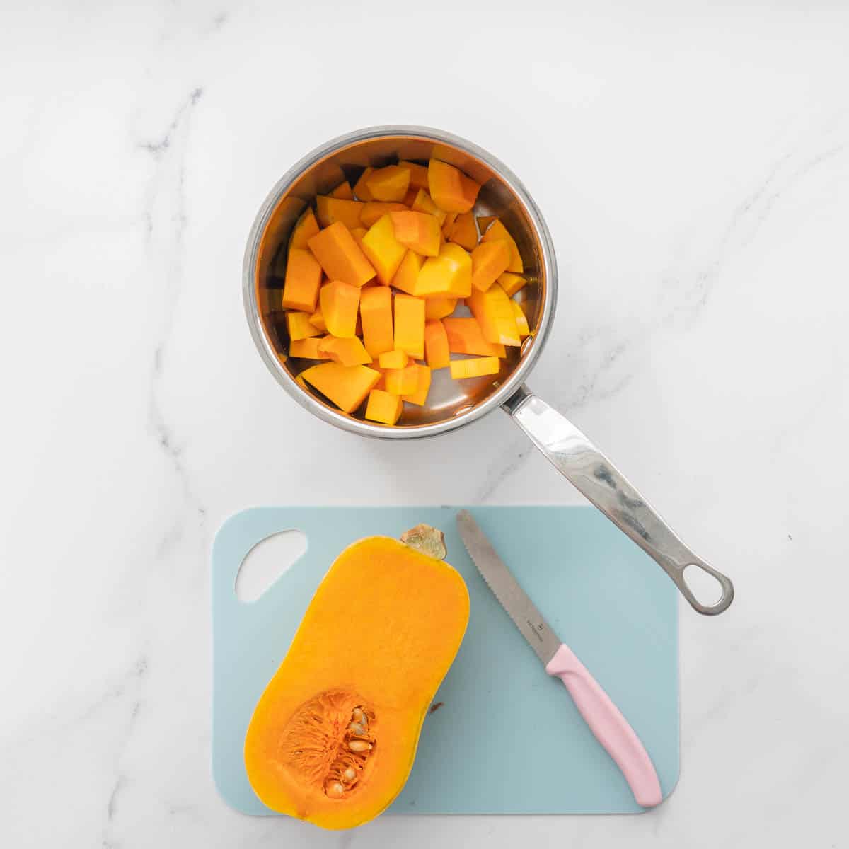 Half a butternut squash on a chopping board next to a pot of cubed butternut.