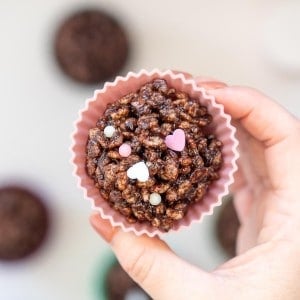 A chocolate crackle in a pink cupcake liner with pink and white heart shaped sprinkles.