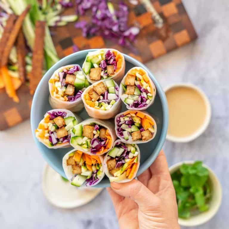 A plate full of rice paper rolls with there colourful vegetable fillings visible being held up to the camera.