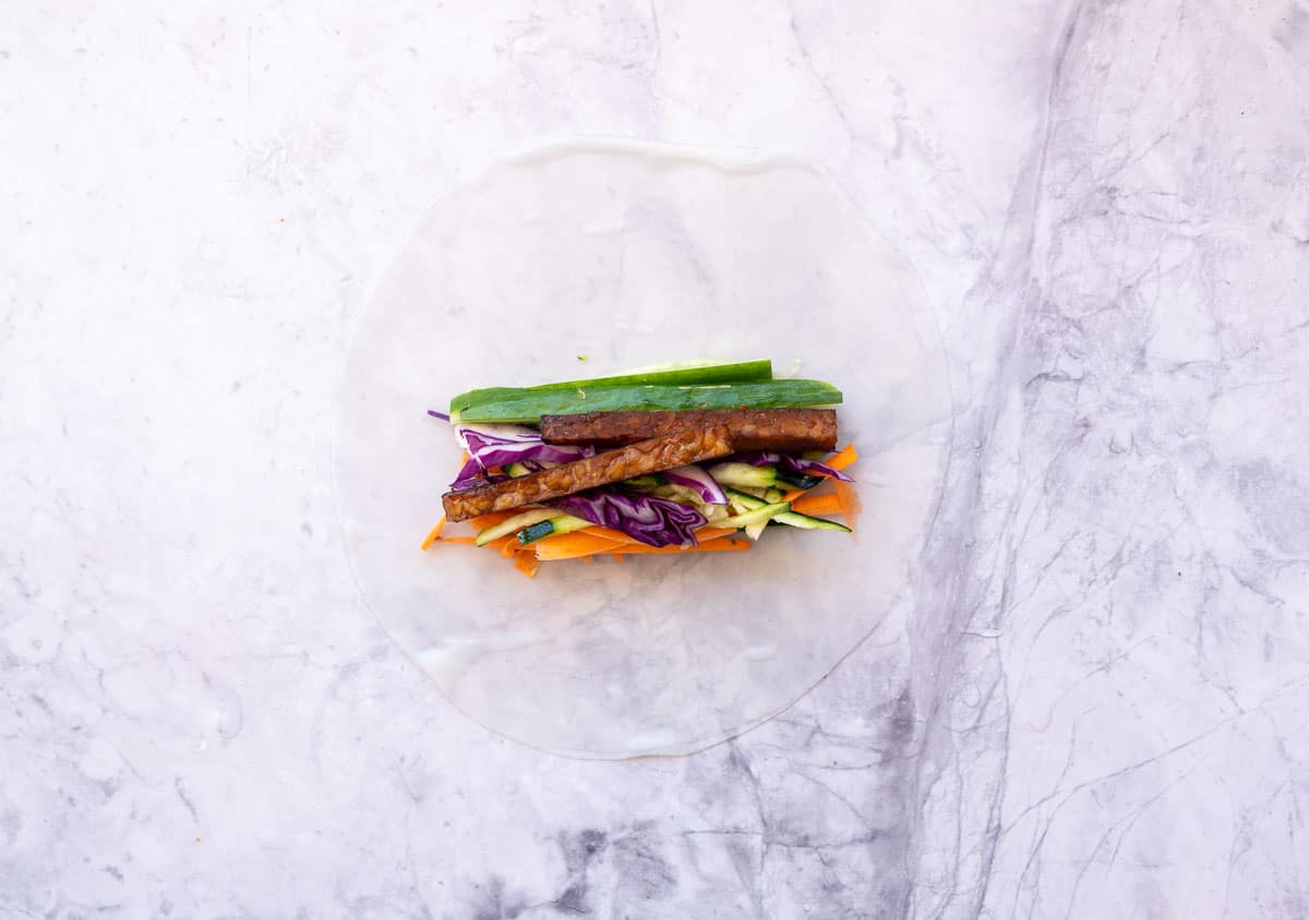 Rice paper laid on bench top with vegetables stacked together.