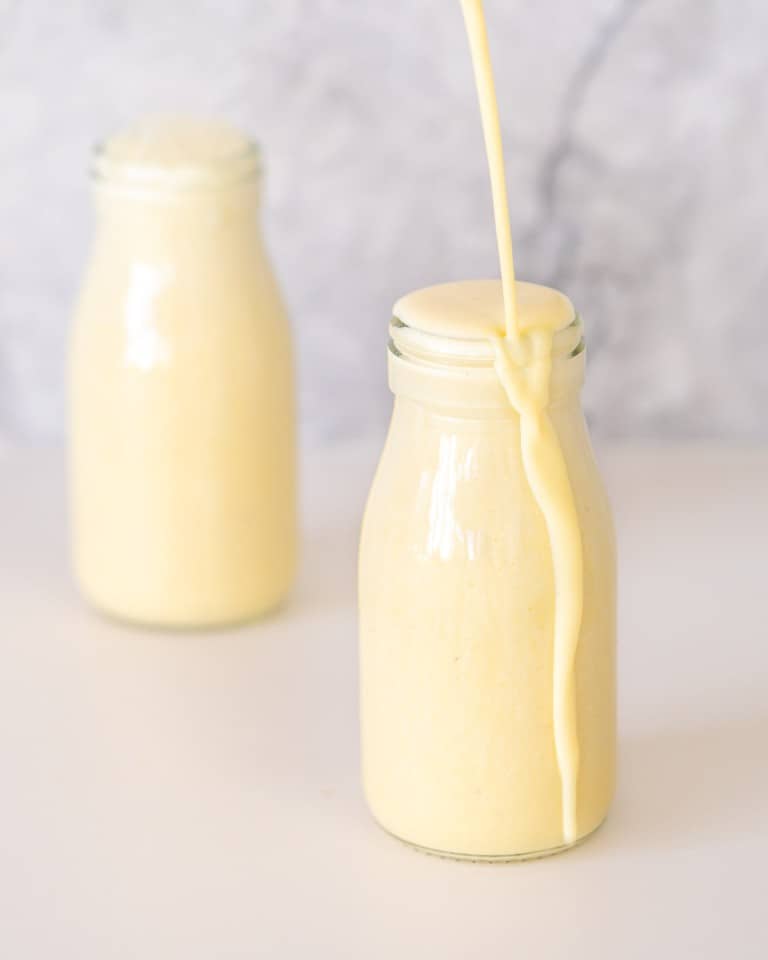 Banana milk being poured into a small glass bottle until it overflows.
