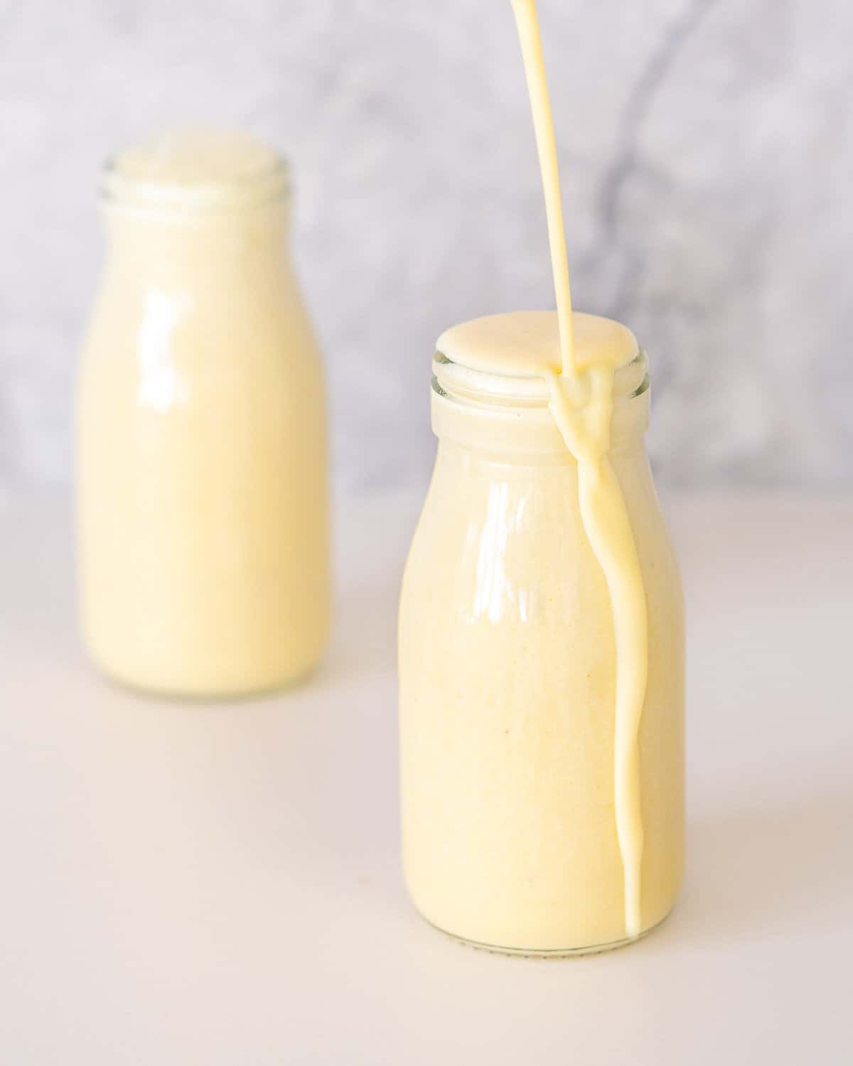 Banana milk being poured into a small glass bottle until it overflows.