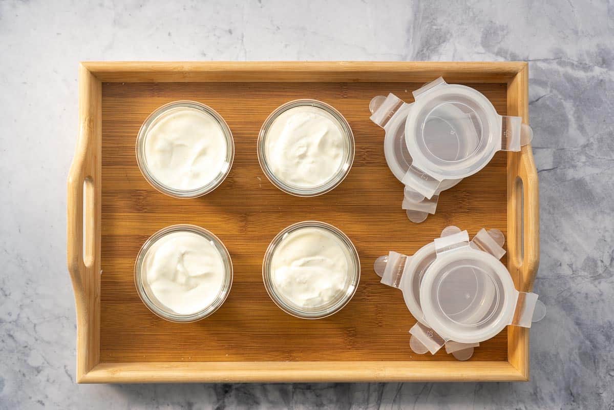 Four small glass jars half filled with yogurt.