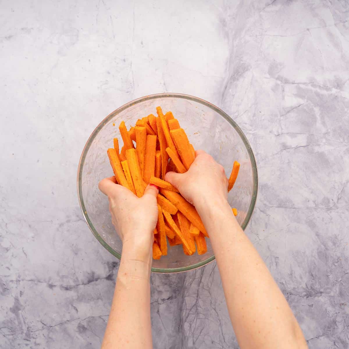 Hand in a mixing bowl rubbing paste onto carrot sticks.