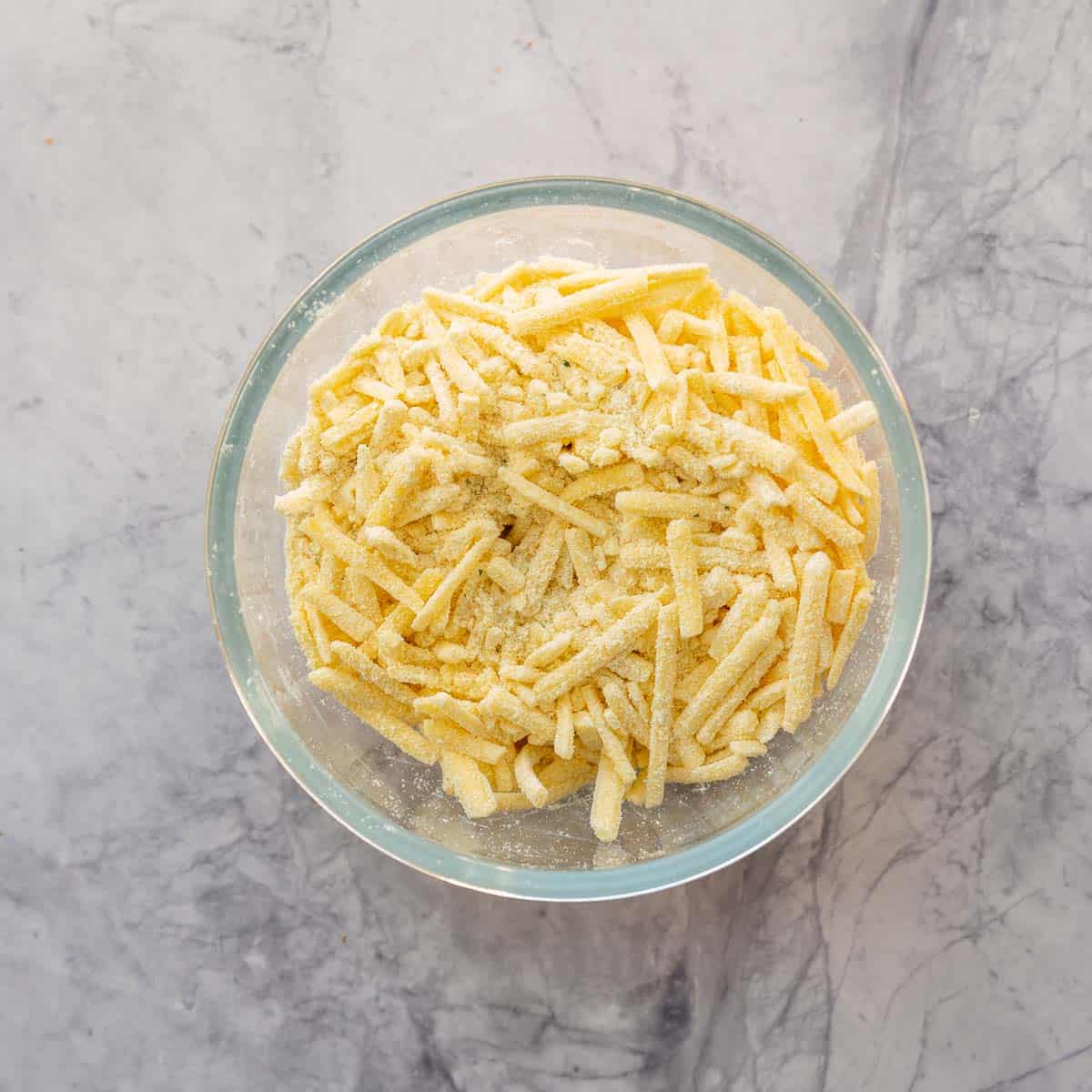 A glass mixing bowl filled with grated cheese coated in powdered soup mix.
