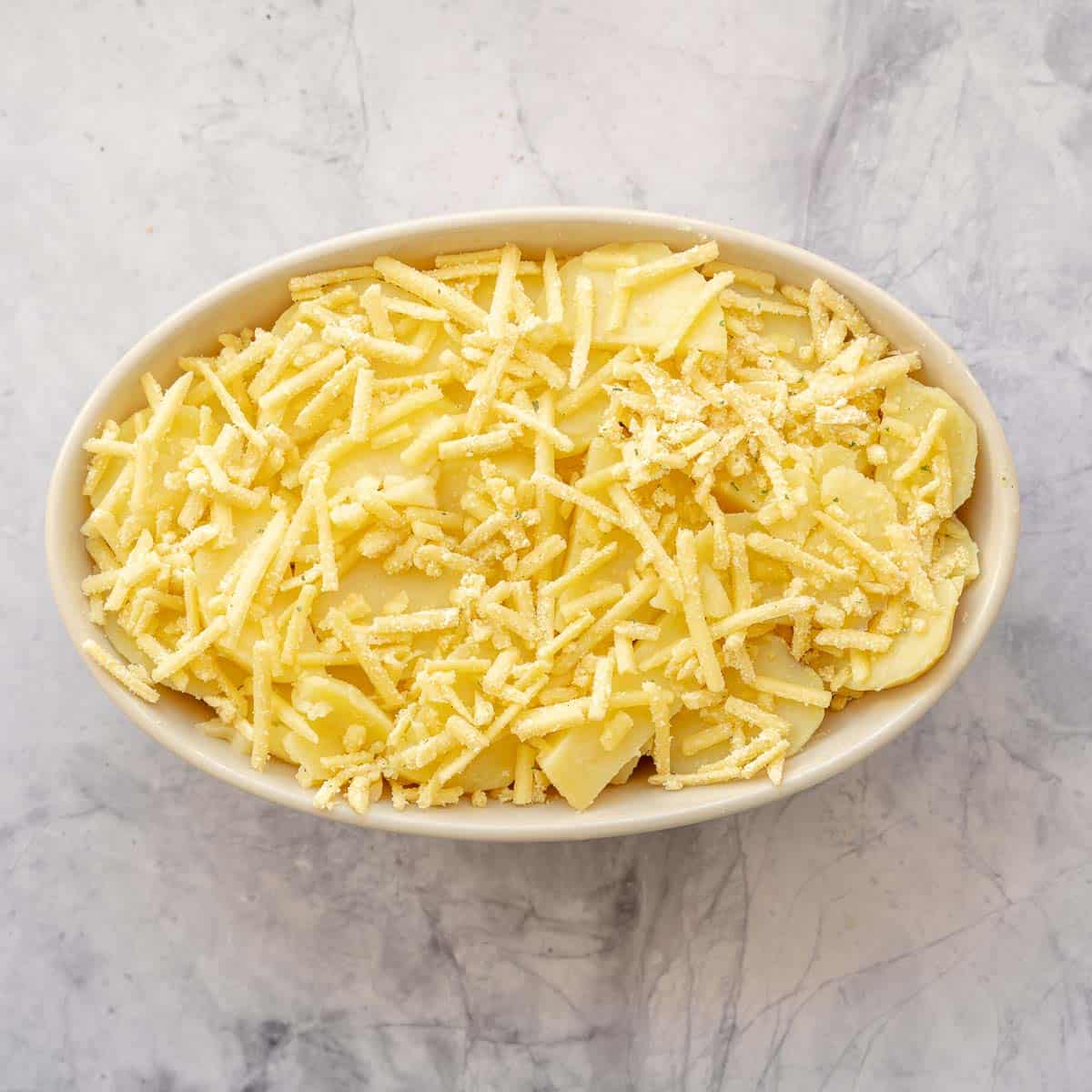 Sliced potatoes layered in a baking dish with grated cheese.