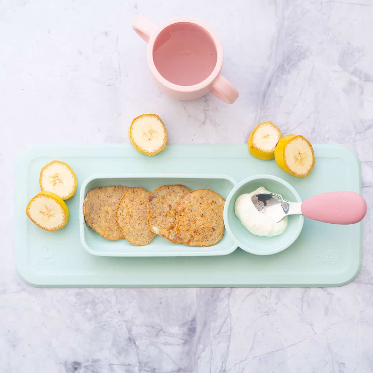 Baby plate with small pancakes and a dish of yogurt with a pink handled spoon.
