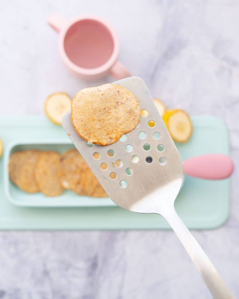 A baby pancake being held up to the camera on a stainless steel spatula.
