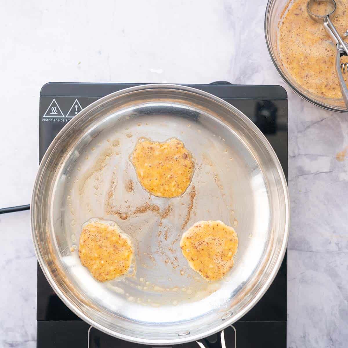 Three small dollops of pancake batter on a greased frying pan.