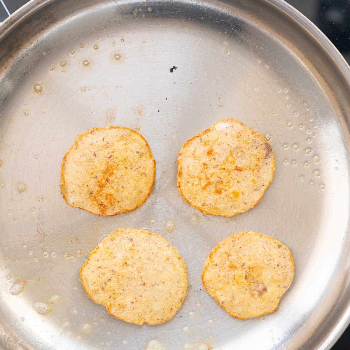 four baby pancakes in a stainless steel pan.