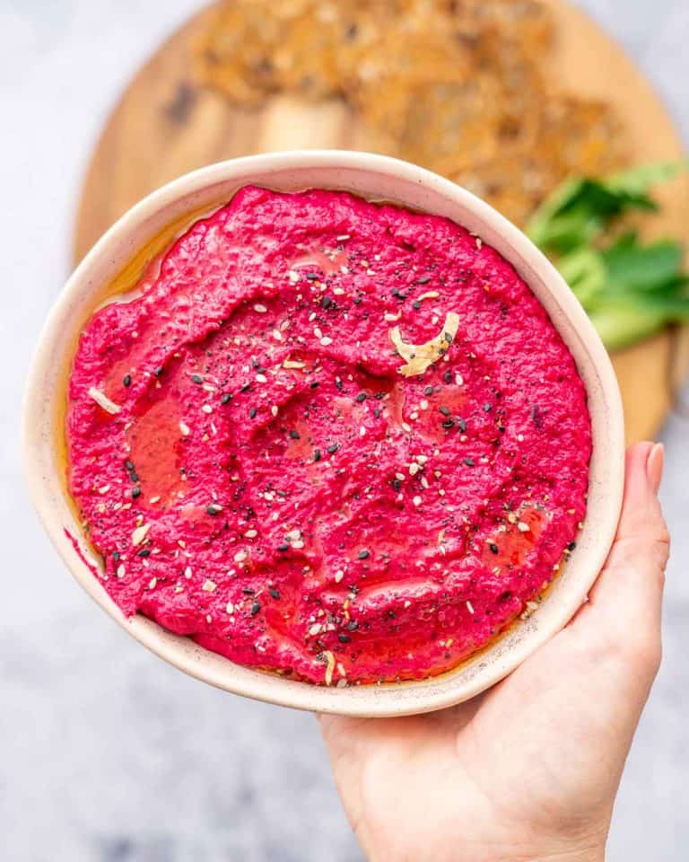 A bowl of bright magenta hummus being held up to the camera