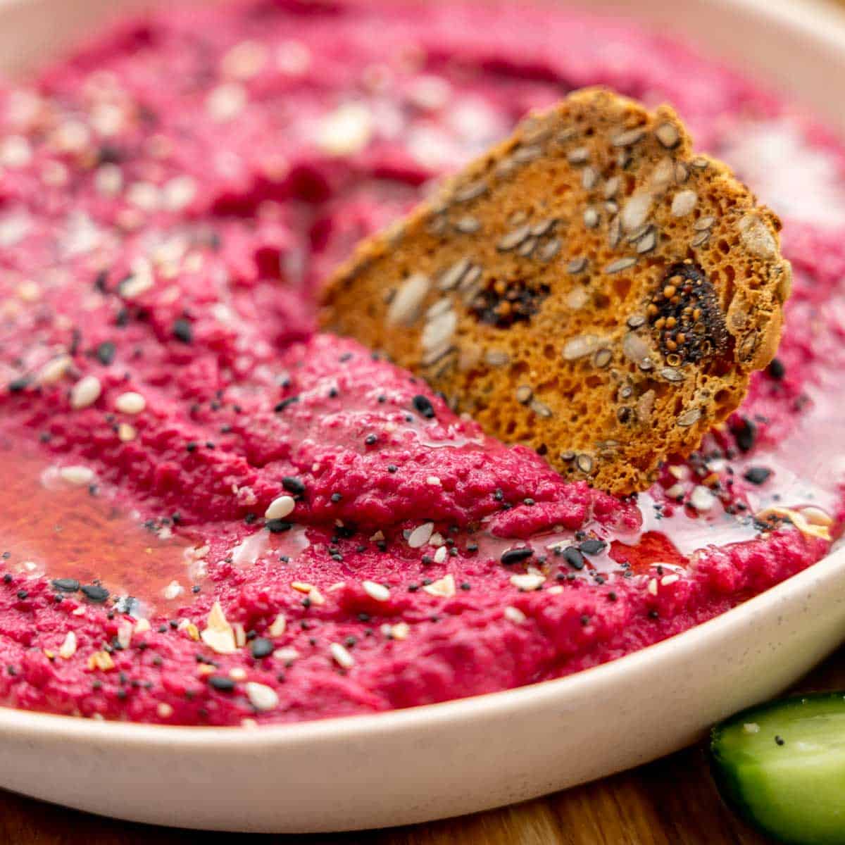 A cracker dunked in a bowl full of beetroot hummus