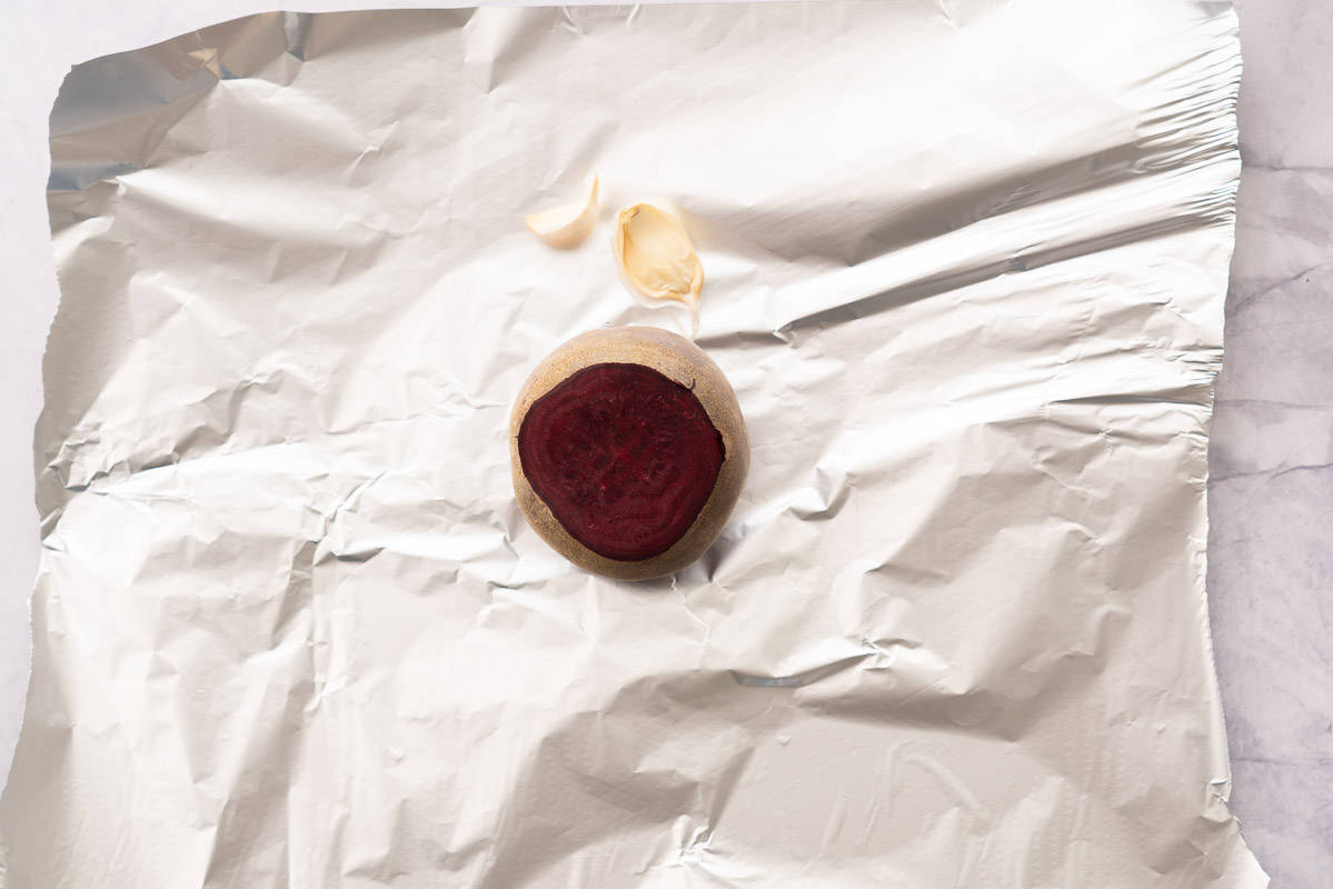 A topped beetroot and two cloves of garlic sitting on a sheet of tinfoil