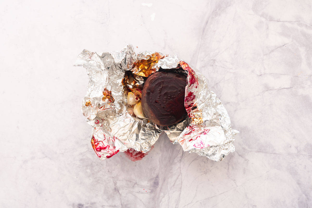 Cooked beetroot and garlic unwrapped in a sheet of tinfoil sitting on the bench.