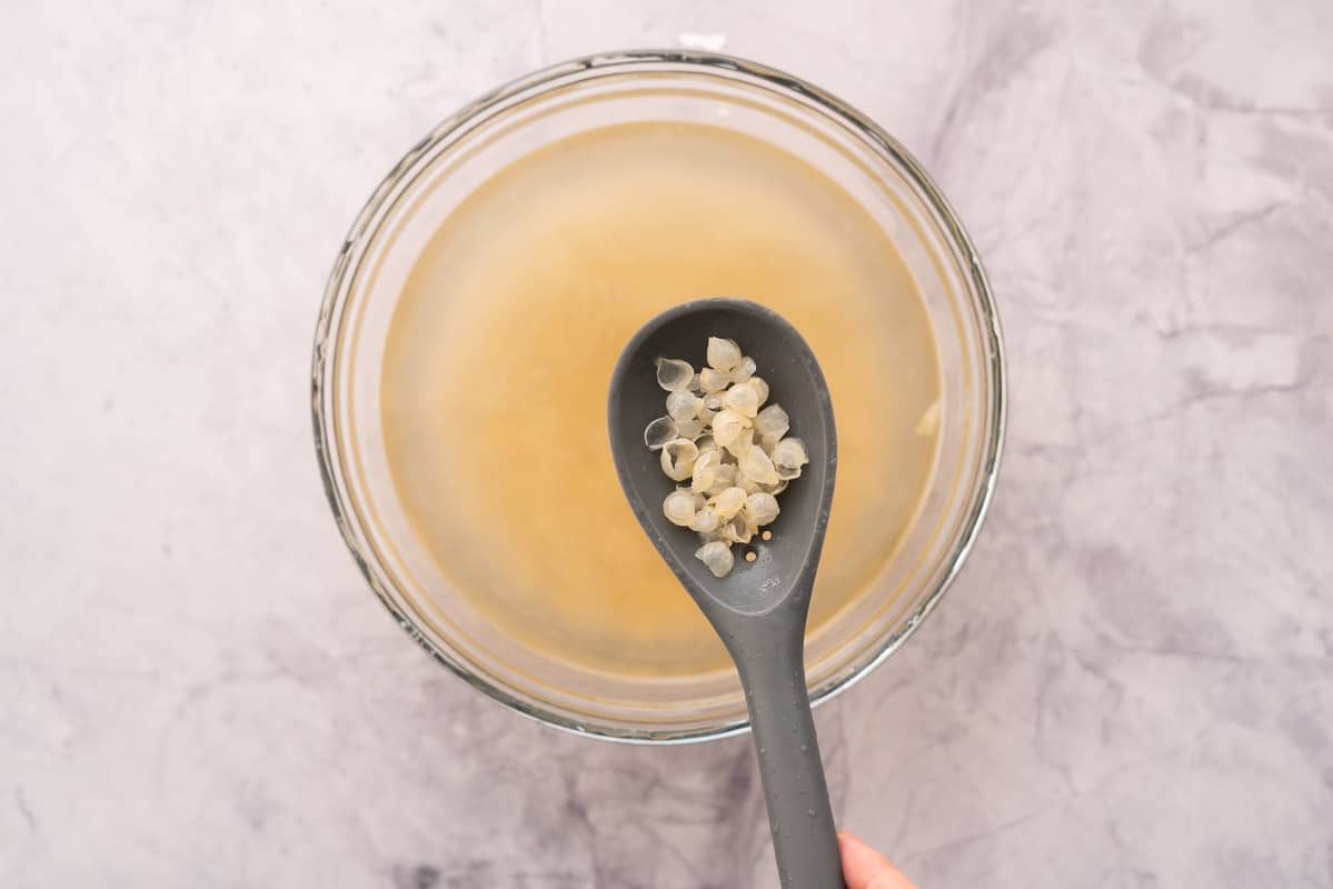 A spoon full of chickpea skins held above a bowl full of chickpeas in a large bowl of water