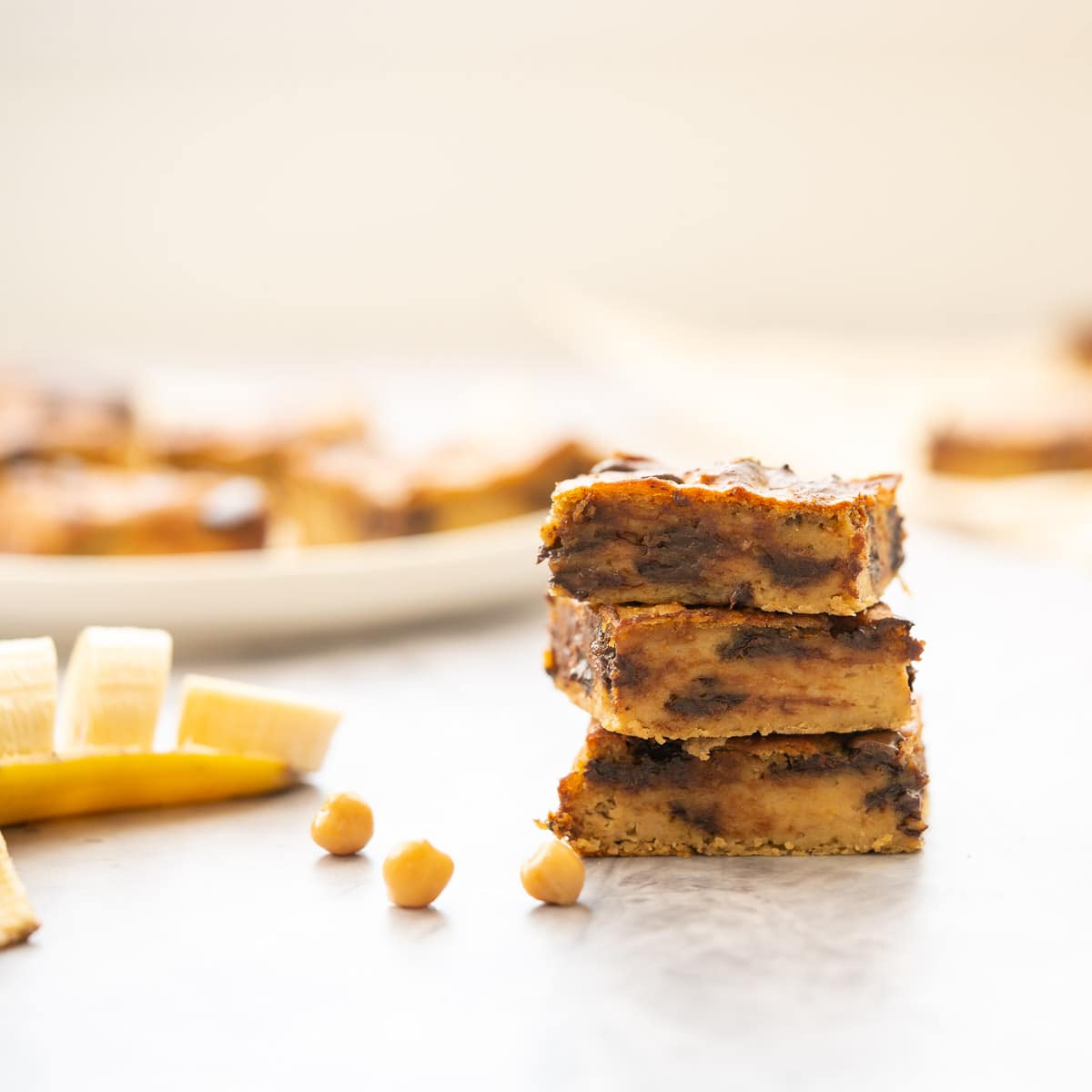 Stack of sliced chickpea brownie on the bench next to a sliced banana and plateful of brownie 