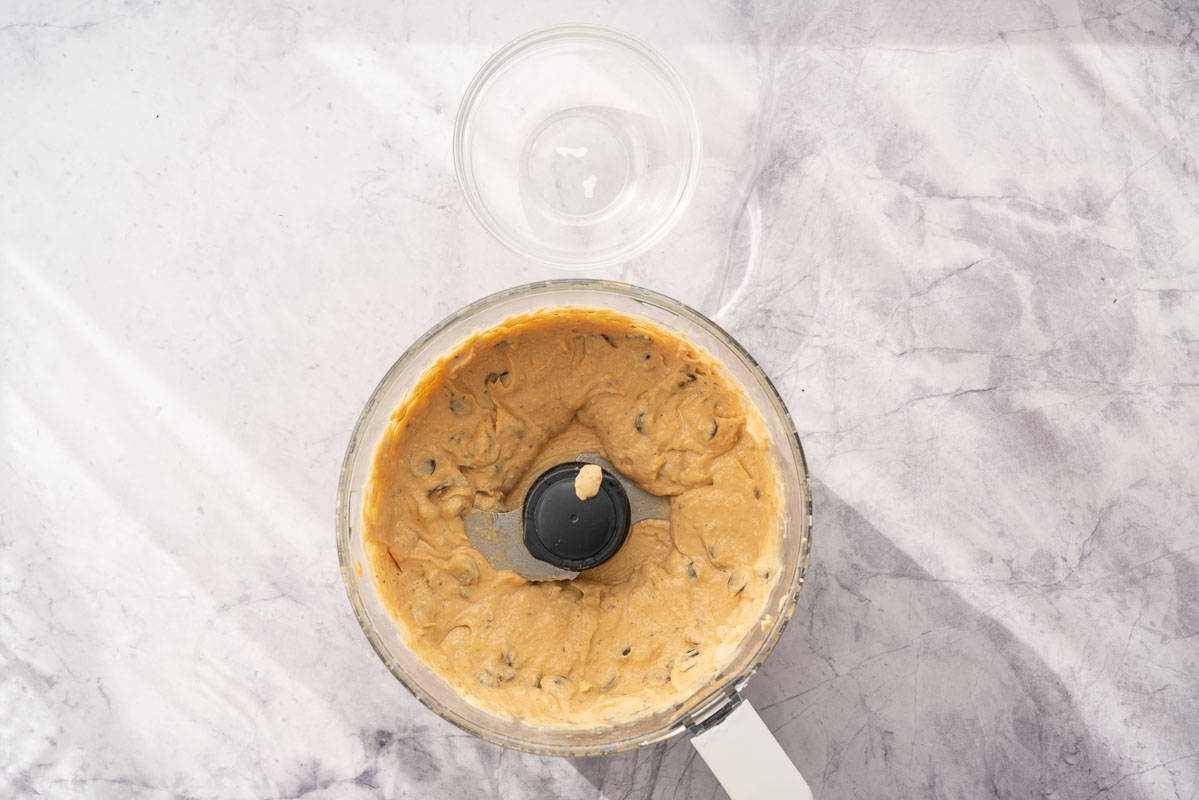 A food processor sitting on the bench with ingredients whizzed together inside of it with chocolate chips added to it.