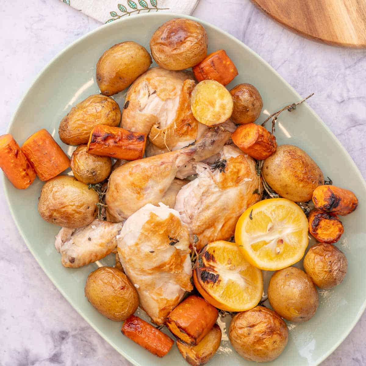 A large mint green serving dish filled with roasted potatoes, carrots and chicken sitting on the bench in front of the crockpot