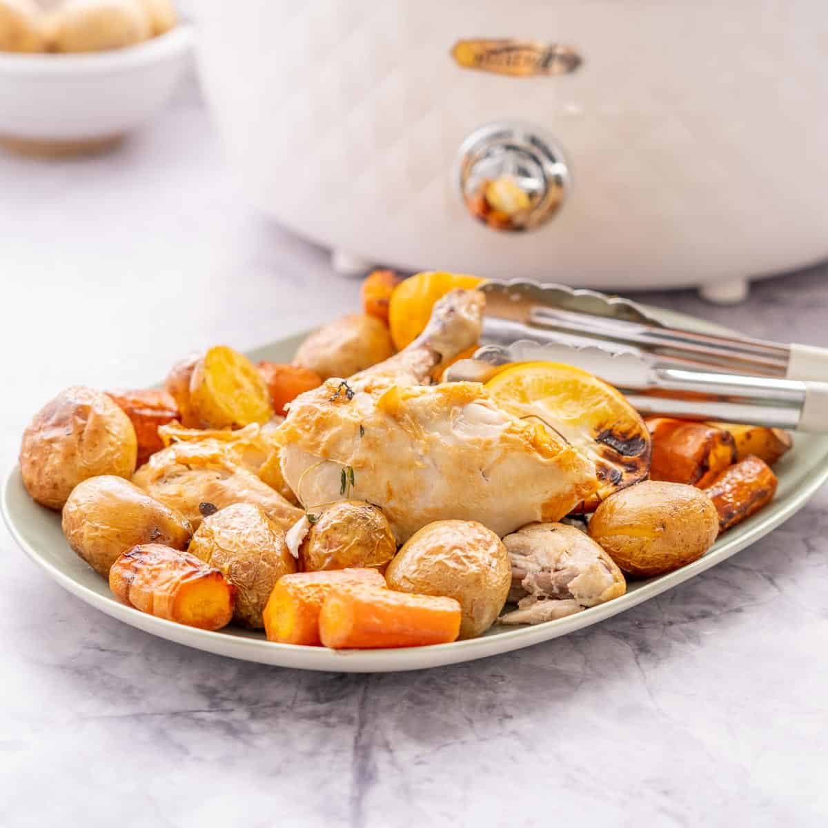 A platter of roasted chicken and vegetables sitting in front of a slow cooker.