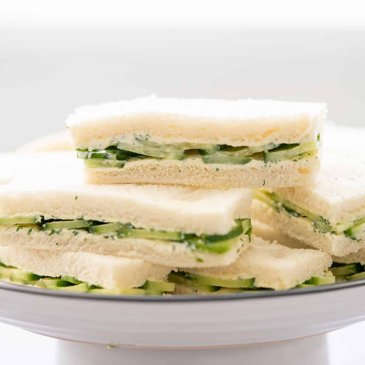 Cucumber cream cheese sandwiches stacked on top of one another.