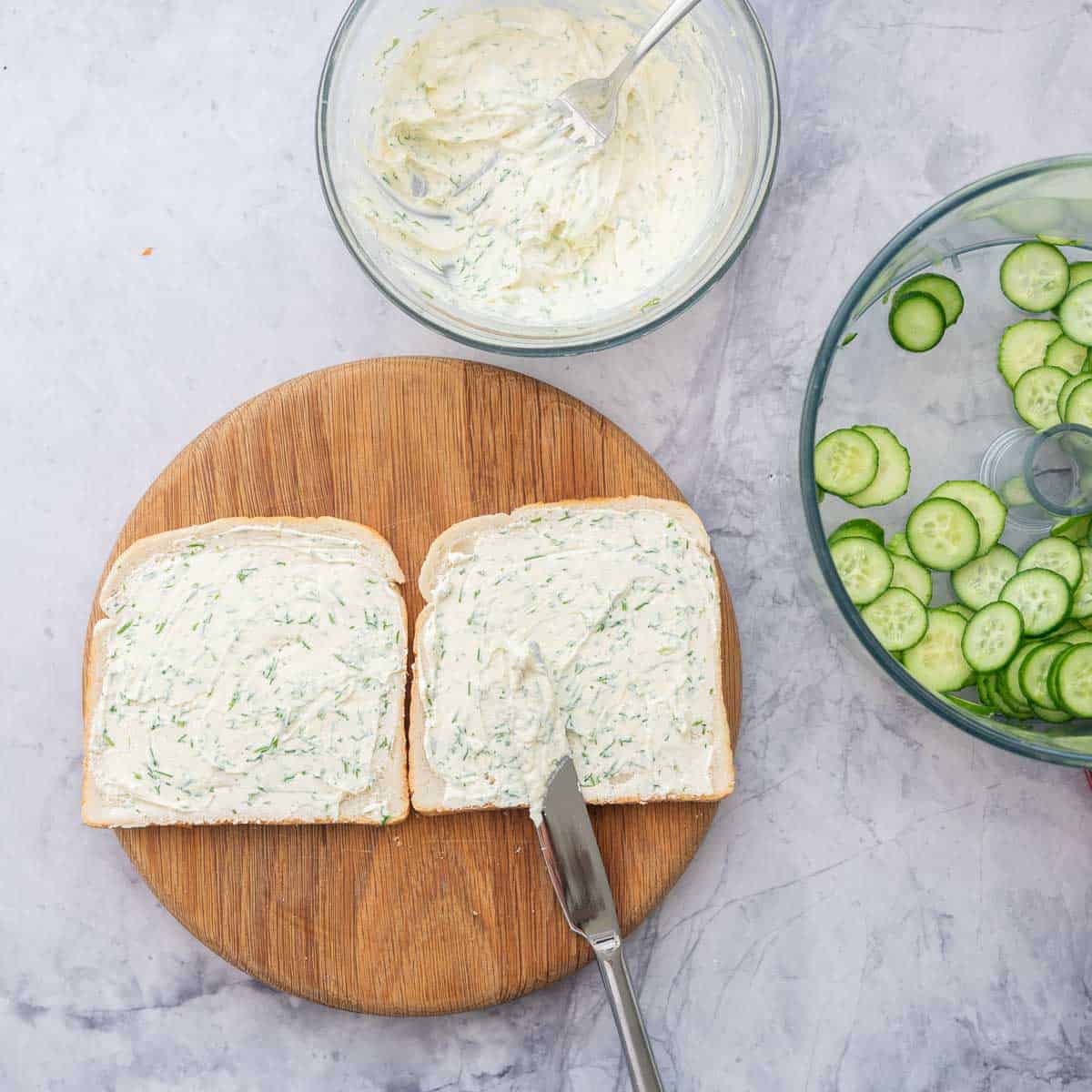 Cream cheese mixture being spread with knife onto two pieces of bread.