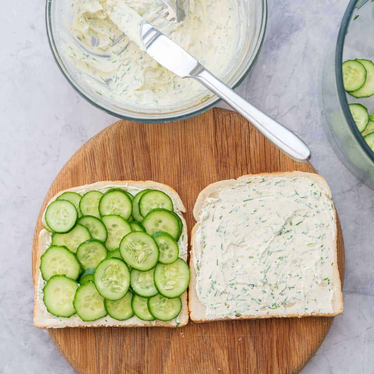 One piece of bread layered with slices of cucumbers on top of cream cheese mixture.