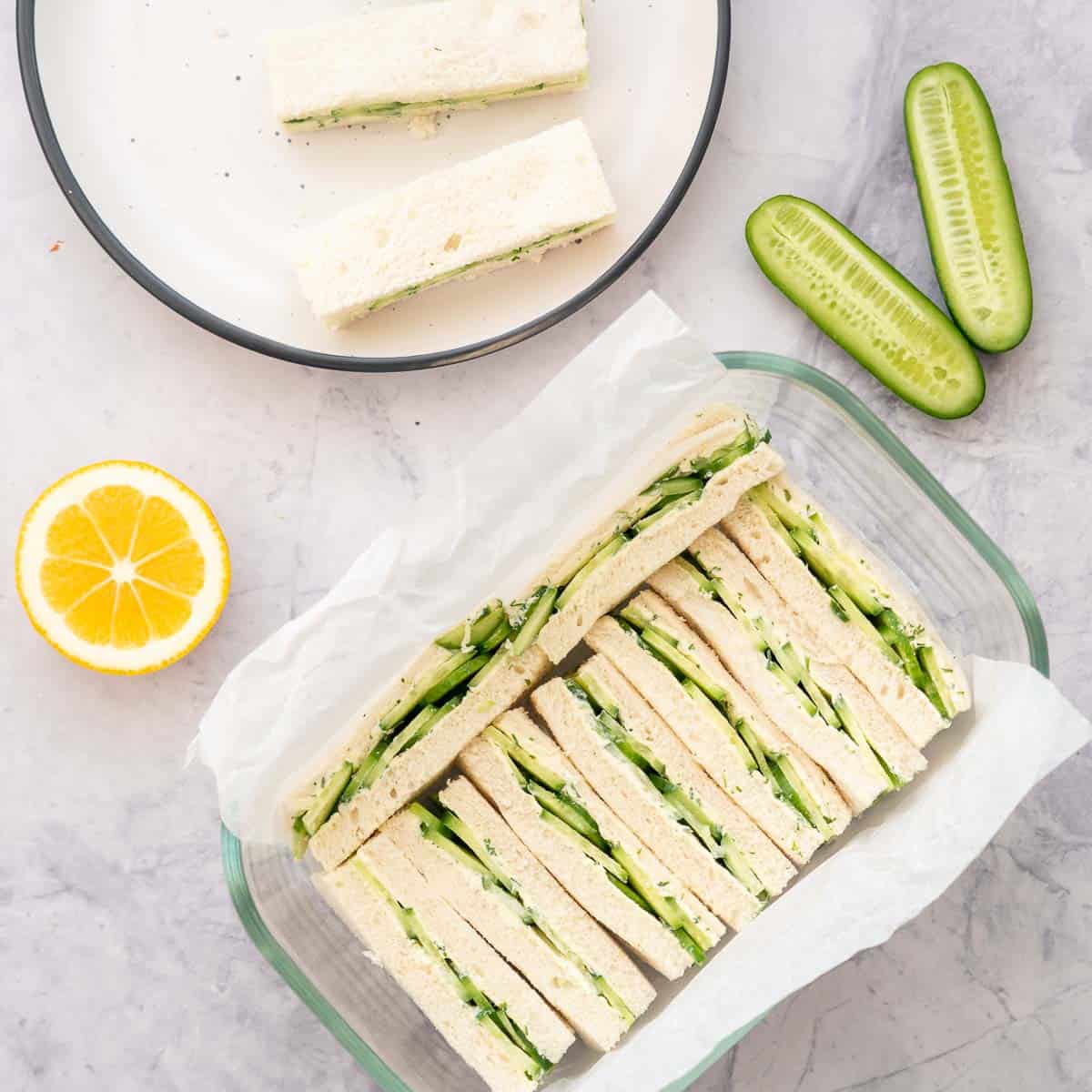 Cream cheese sandwiches in glass container, plate with sandwiches on it.