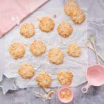 12 golden cookies on creased baking paper with a pink tea towel beside it