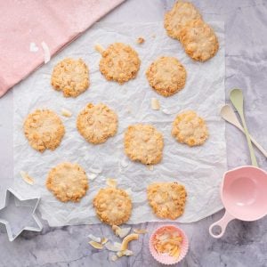 12 golden cookies on creased baking paper with a pink tea towel beside it